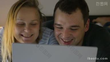 年轻夫妇晚上躺在床上用笔记本电脑在网上看幽默节目或<strong>搞笑视频</strong>